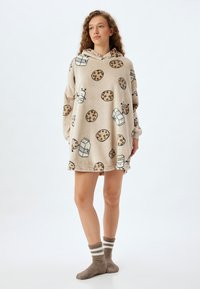 Vestido de dormir con capucha en color beige, hecho de suave forro polar, con ilustraciones de galletas y leche, mangas largas y un corte holgado. Incluye calcetines.