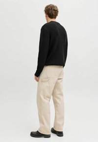 Czarny sweter dzianinowy z długimi rękawami, zestawiony z beżowymi spodniami. Strój charakteryzuje się luźnym krojem, prążkowaną teksturą i solidnym czarnym obuwiem.