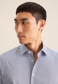 Blauwe en witte gestreepte shirt met een button-down kraag, geometrisch patroon en textuurstof. Close-up van de schouder en halslijn.