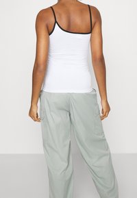 Biały top na ramiączkach z czarnymi wykończeniami, dopasowany krój. W zestawie z luźnymi, jasnobylawymi spodniami cargo z bocznymi kieszeniami.