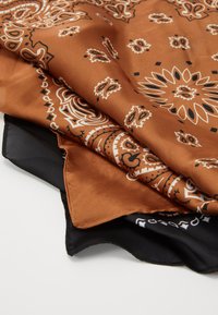 Brauner Satin-Schal mit weißen Paisley- und geometrischen Mustern, gefaltet mit einem schwarzen Rand. Glatte Textur und elegante Designdetails.