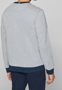 Sweat-shirt gris à col rond avec une texture côtelée, poignets et taille bleu marine, présentant un détail de col rayé contrastant.