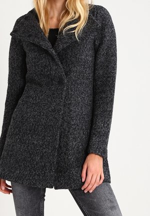 Femme portant un manteau en laine texturée gris foncé à boutons croisés et col large, associé à un jean gris.