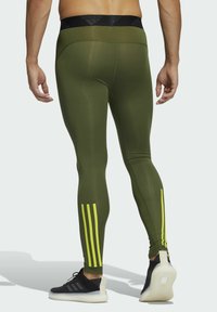 Zielone legginsy sportowe z czarnym pasem w talii i trzema pionowymi, neonowożółtymi paskami na dolnej części nóg. Gładki, elastyczny materiał.