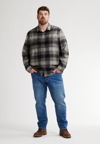 Grijs en zwart geruite flanellen overhemd met borstzakken, vergezeld van blauwe jeans en bruine schoenen. Rechte pasvorm, zichtbare stiksels.
