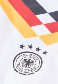 Fudbalska majica Njemačke sa bijelom pozadinom, smjelim crvenim, žutim i crnim dijagonalnim prugama, te grbom crnog orla s pet zvjezdica iznad.