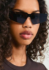 Black rectangular sunglasses with a thick frame, featuring a matte finish and subtle silver hardware details.