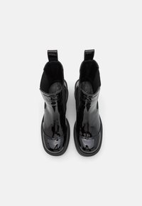 Botas de tobillo de charol negro con paneles elásticos en los lados, puntas redondeadas y lengüetas en la parte posterior. Textura suave y acabado brillante.
