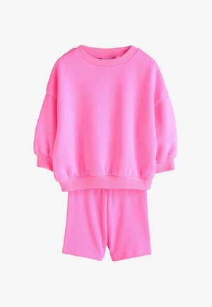 Ryškiai rožinis megztinis su ilgomis rankovėmis ir derančios ribinės šortai, pateikti ant balto fono.