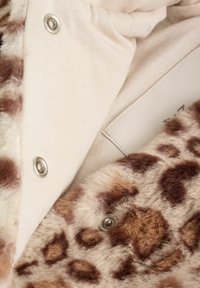 Țesătură cu imprimeu de leopard, cu o textură moale, având căptușeală interioară bej și nasturi metalici argintii. Modelul de culori este neted și contrastant.