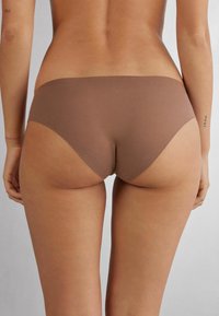 Culotte marron sans couture avec une taille basse, texture lisse, et couverture minimale, dotée d'un bord propre sans coutures ni étiquettes visibles.