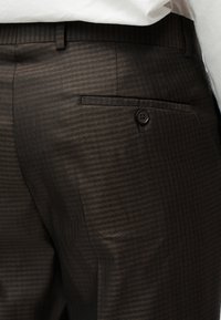 Καφέ παντελόνι με σχέδιο και υφή, με πλαϊνή τσέπη και κουμπί κλεισίματος, κατασκευασμένο από ελαφρύ, δομημένο ύφασμα.