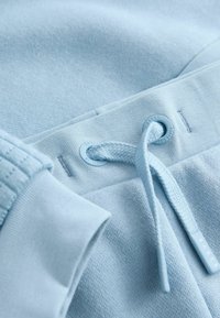 Lyseblå sweatshirts detalje med struktureret stof, flade sømme, snor med justerbart stop og et stofmærke mærket "BAKER."