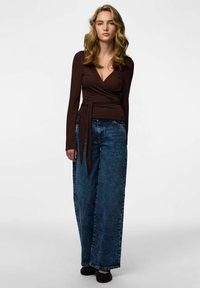 Brun långärmad omlott-topp med V-ringning, kombinerad med vida, blekta blå jeans och svarta ballerinaskor. Mjukt tyg.