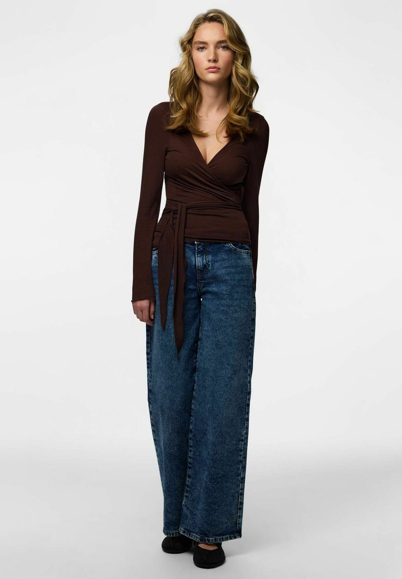 Brun långärmad omlott-topp med V-ringning, kombinerad med vida, blekta blå jeans och svarta ballerinaskor. Mjukt tyg.