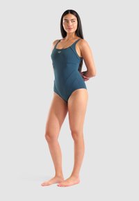 Maillot de bain une pièce en bleu sarcelle, fabriqué à partir d'un matériau extensible. Présente des bretelles larges et un design épuré avec des accents de coutures.