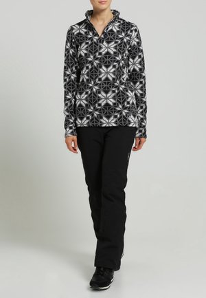 Pull en polaire avec un motif géométrique noir et blanc, col montant et fermeture éclair. Associé à un pantalon noir et des chaussures noires. Texture lisse.