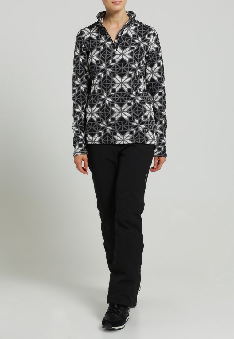 Fleece-Pullover im schwarz-weißen geometrischen Muster, hoher Kragen und Reißverschluss. Kombiniert mit schwarzen Hosen und schwarzem Schuhwerk. Glatte Textur.