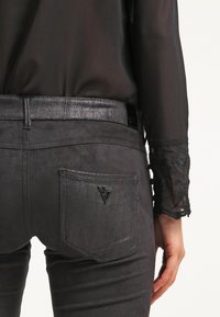 Donkergrijze broeken met een gestructureerde afwerking, voorzien van een driehoekige logo-applicatie op de achterzak en een slanke zwarte riem met een gestructureerd ontwerp.
