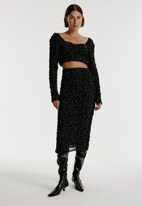 Zwart gerimpeld tweedelig outfit met lange mouwen, cropped top en rok met witte stippen. Glanzende zwart kniehoge laarzen.