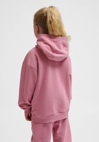Rosa hoodie i mjukt tyg med en avslappnad passform, med en stor huva och ribbade ärmslut. Designen är enkel utan synliga mönster eller detaljer.