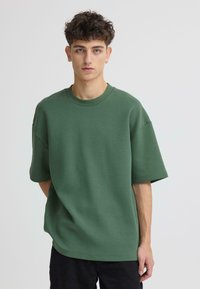 T-shirt vert oversize en tissu doux, doté d'un col rond et de manches courtes. Design simple sans motifs ni accents visibles.