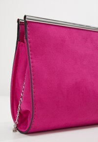 Fuchsiová semišová psaníčko s stříbrným kovovým horním zapínáním, řetízkovým popruhem a prošitými detaily pod�él okrajů, s hladkou texturou.