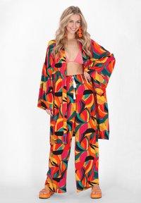 Kleurrijke, gemusterde strandkleding set met een lange kimono-achtige omslag en losse broeken, in levendige tinten van rood, oranje en groen.