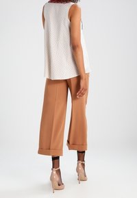 Vit ärmlös topp med svarta prickar, kombinerad med lösa bruna byxor och nude höga klackar. Strukturerade nätstrumpor synliga.