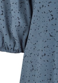 Tessuto blu con una superficie texturizzata presenta motivi a macchie nere, dettagli con polsini arricciati e una qualità morbida e drappeggiata.