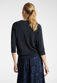 Maglione a maglia blu navy con maniche a tre quarti, leggero luccichio e orlo a coste. Abbinato a una gonna scura a fantasia blu.