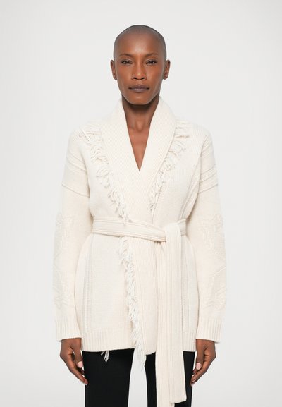 Cardigan beige en tricot avec un col châle, des détails à franges, des manches larges et une taille nouée. Caractéristiques de motifs texturés sur le tissu.