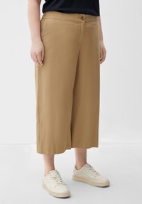 Light brown, wide-leg trousers with a smooth texture, featuring a front button closure and side pockets. Paired with white sneakers.