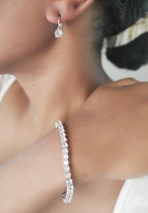 Gioielli color argento con un bracciale scintillante adornato da multiple pietre tonde e orecchini pendenti abbinati con un accento in pietra singola.