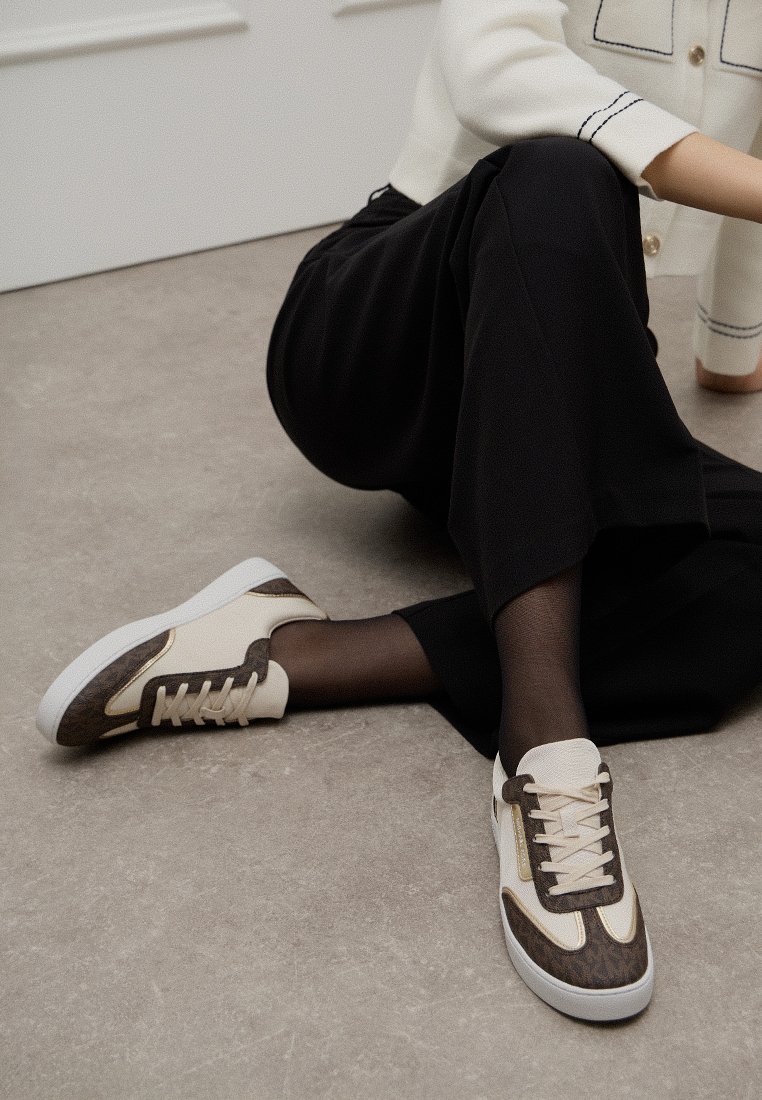 Baskets sportives avec une combinaison de couleurs blanche et marron, présentant un côté marron texturé, des lacets crème et une semelle extérieure blanche.