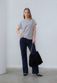 Striped cotton t-shirt in white and navy, paired with dark blue flared jeans. Model holds a black suede bag with a chain strap and wears black heels.