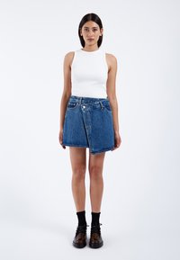 Gonna in denim con orlo grezzo, dettaglio delle tasche frontali e colore blu sbiadito. Abbinata a una canotta bianca attillata e calze nere.