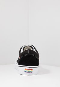 Sorte semsket sneaker med hvit gummisåle, med kontrasterende hvit søm og en regnbue "Off the Wall" logo på hælen.