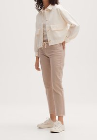 Una chaqueta crema recortada con grandes bolsillos de parche, combinada con pantalones rectos rosa claro y zapatillas blancas; tejido de algodón.