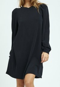 Svart långärmad klänning med avslappnad passform, rund halsringning, mjukt tyg och subtila puffärmar. Slät yta och längd till mitten av låret.