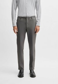 Pantalon gris slim-fit avec une texture lisse, doté d'une fermeture éclair, de poches latérales et d'une passante pour ceinture. Associé à des mocassins noirs.