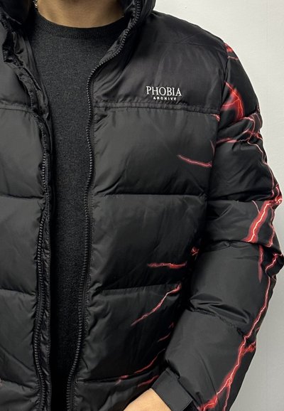 Giacca a vento nera con sezioni a rombi orizzontali, caratterizzata da motivi a zig-zag rossi e una chiusura con zip. Logo "PHOBIA ARCHIVE" visibile.