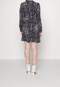 Černé šaty s bílým zebřím potiskem, dlouhé rukávy, se staženým pasem a sukní nad kolena; doplněné bílými kotníkovými botami s čtveratými podpatky.