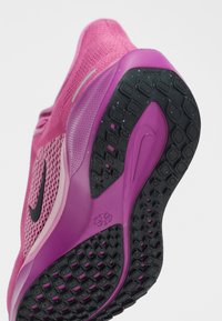 Chaussure de sport rose et violette avec une semelle noire texturée avec un logo Nike, vue par le dessous et de côté.