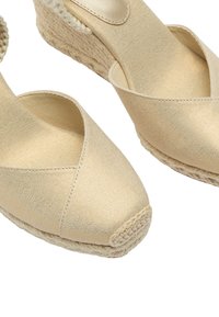 Beżowe espadryle na koturnie z krzyżowym paskiem, plecionymi podeszwami z juty oraz fakturowanym materiałem, z gładkim, błyszczącym akcentem na obcasie.