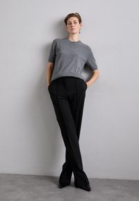 Szürke, rövid ujjú pulóver fekete, szabott nadrággal párosítva. Az öltözék puha textúrával és elegáns, testhezálló fazonnal rendelkezik.