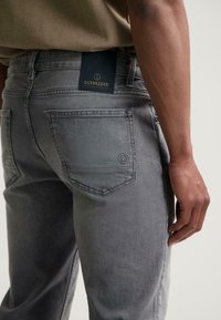 Szürke denim farmernadrág egyenes szabással, hátul bőr címkével, amelyen az "DSTREZZED" felirat szerepel, valamint diszkrét varrás részletek a zsebeken.