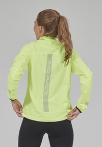 Neon-gelbes, leichtes Laufjacke mit langen Ärmeln, reflektierenden Akzenten und schmalem Schnitt. Mit hohem Kragen und dezentem Branding.