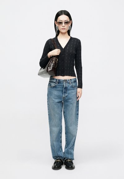 Black knitted cardigan with a V-neck, paired with loose blue jeans. Accessories include sunglasses and a brown handbag. Black shoes complete the look.