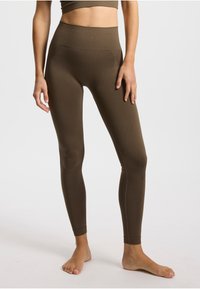 Leggings marron taille haute en tissu extensible, dotés d'un design sans coutures et d'une silhouette ajustée, avec des coutures minimales et sans poches.